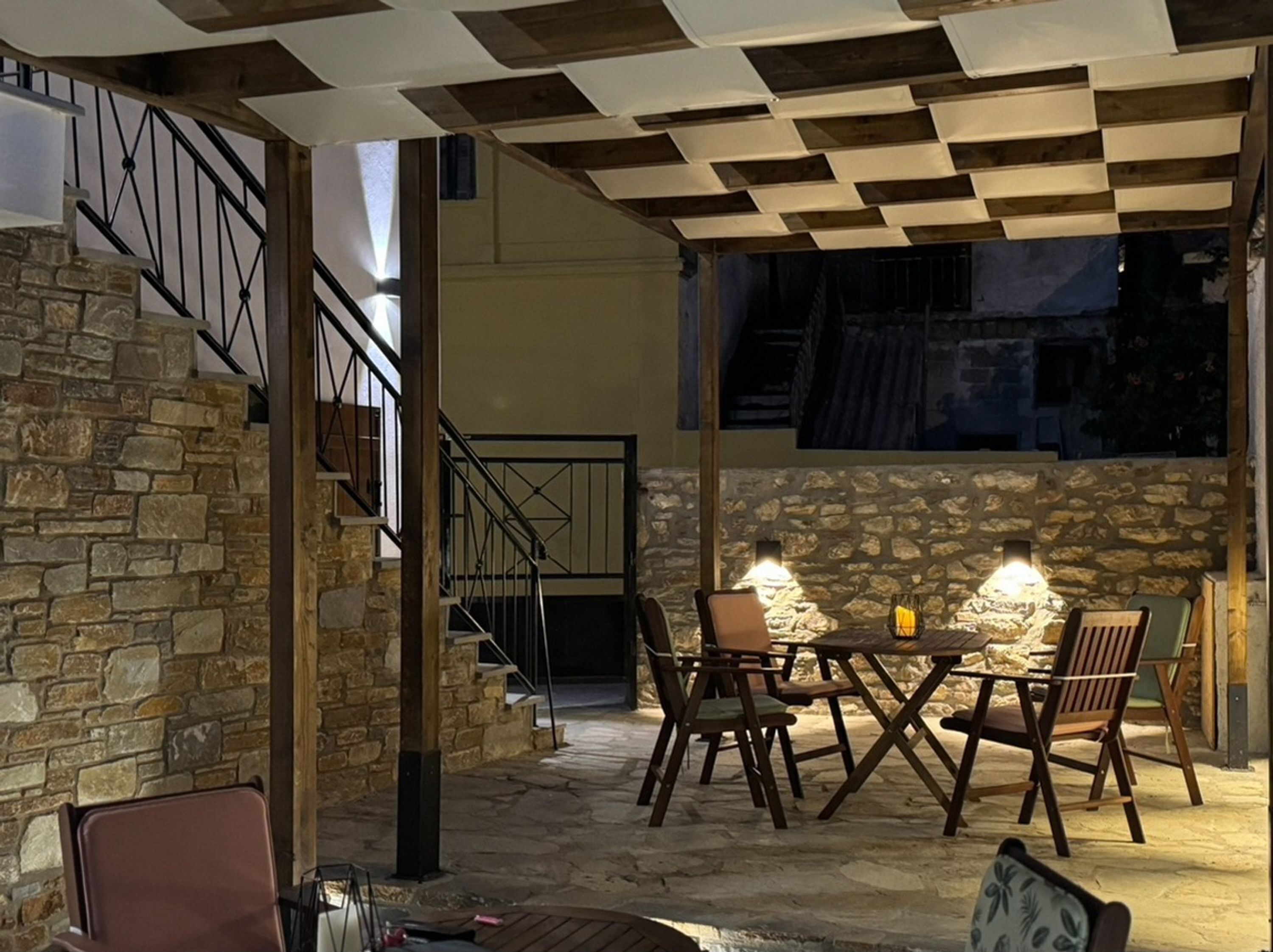 Un espace de détente extérieur accueillant, avec des murs en pierre et un plafond à carreaux, comprenant une table et des chaises sous une lumière chaleureuse.