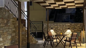 Un espace de détente extérieur accueillant, avec des murs en pierre et un plafond à carreaux, comprenant une table et des chaises sous une lumière chaleureuse.