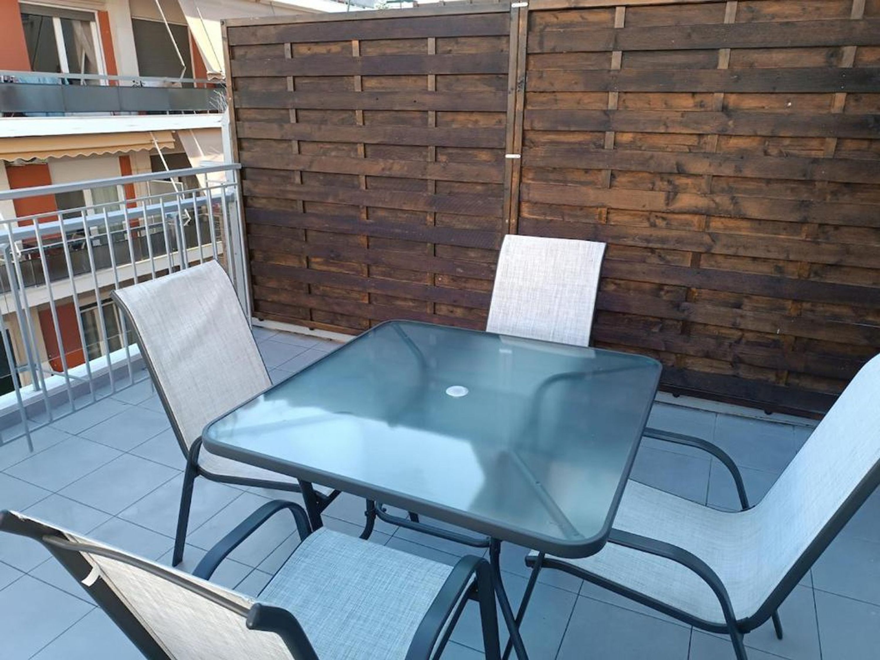 A glass-top table with four chairs on a balcony, a wooden fence, and a metal railing.