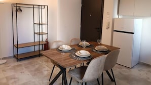 Uma área de refeições com uma mesa de madeira posta para quatro pessoas, quatro cadeiras, uma estante de metal preta, uma porta escura e uma geladeira branca.