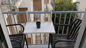Uma varanda com uma mesa pequena e duas cadeiras, com vista para uma área residencial com varandas e árvores.