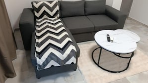 Uma sala de estar moderna com um sofá cinzento, uma manta estampada e uma pequena mesa de centro redonda com um controle remoto.