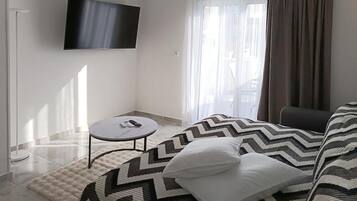 A modern bedroom with a bed, a TV mounted on the wall, a small round table, and a window with curtains.