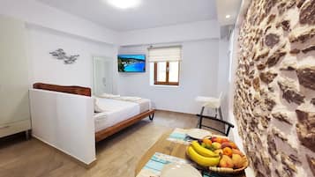 Quarto com uma cama, televisão, janela, parede de pedra e cesta de frutas.