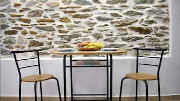 A room with a stone wall, a round wooden table, two metal chairs, and a fruit basket on the table.