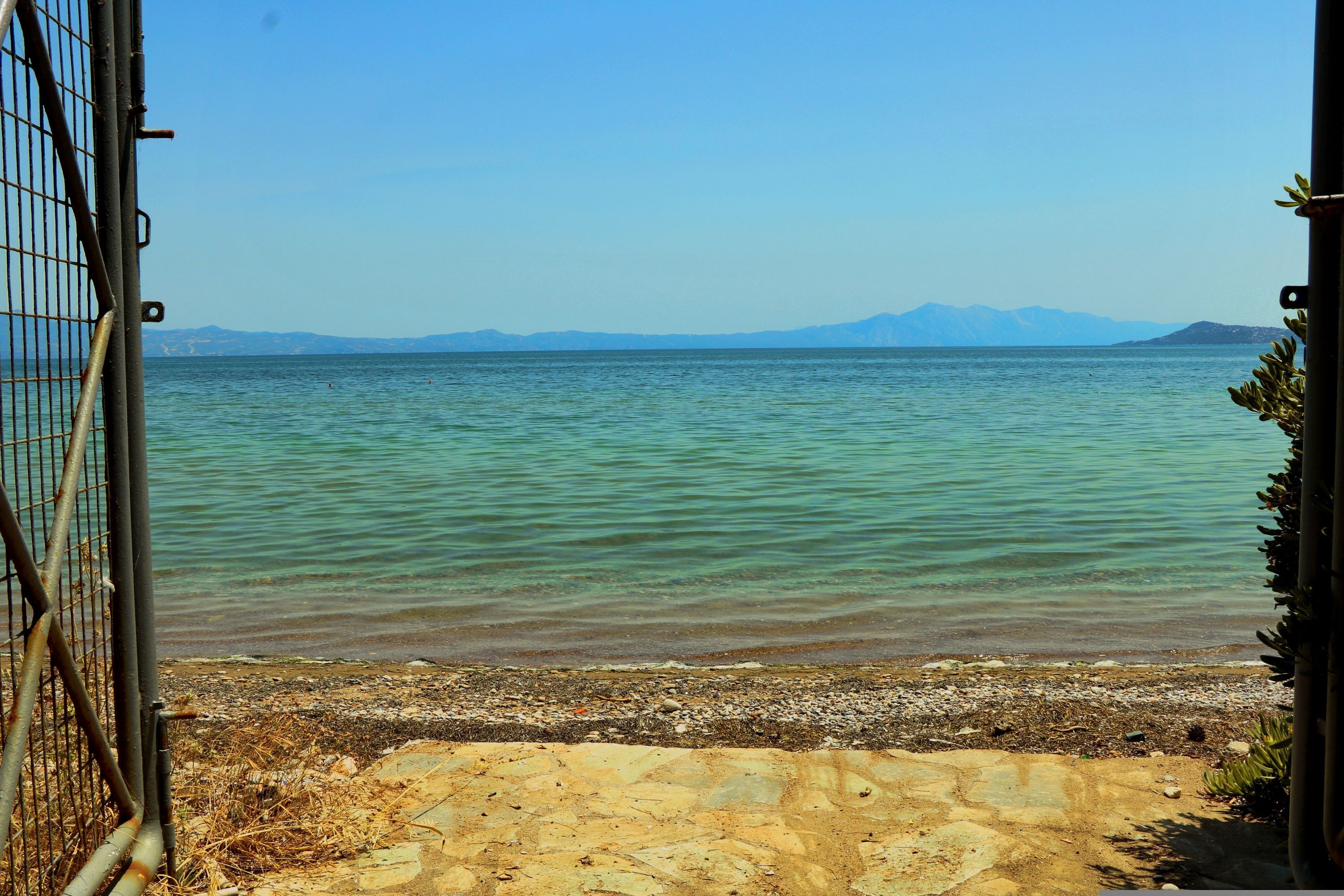 Une vue dégagée sur un lac, avec des montagnes en arrière-plan, une plage de sable et un portail en métal.