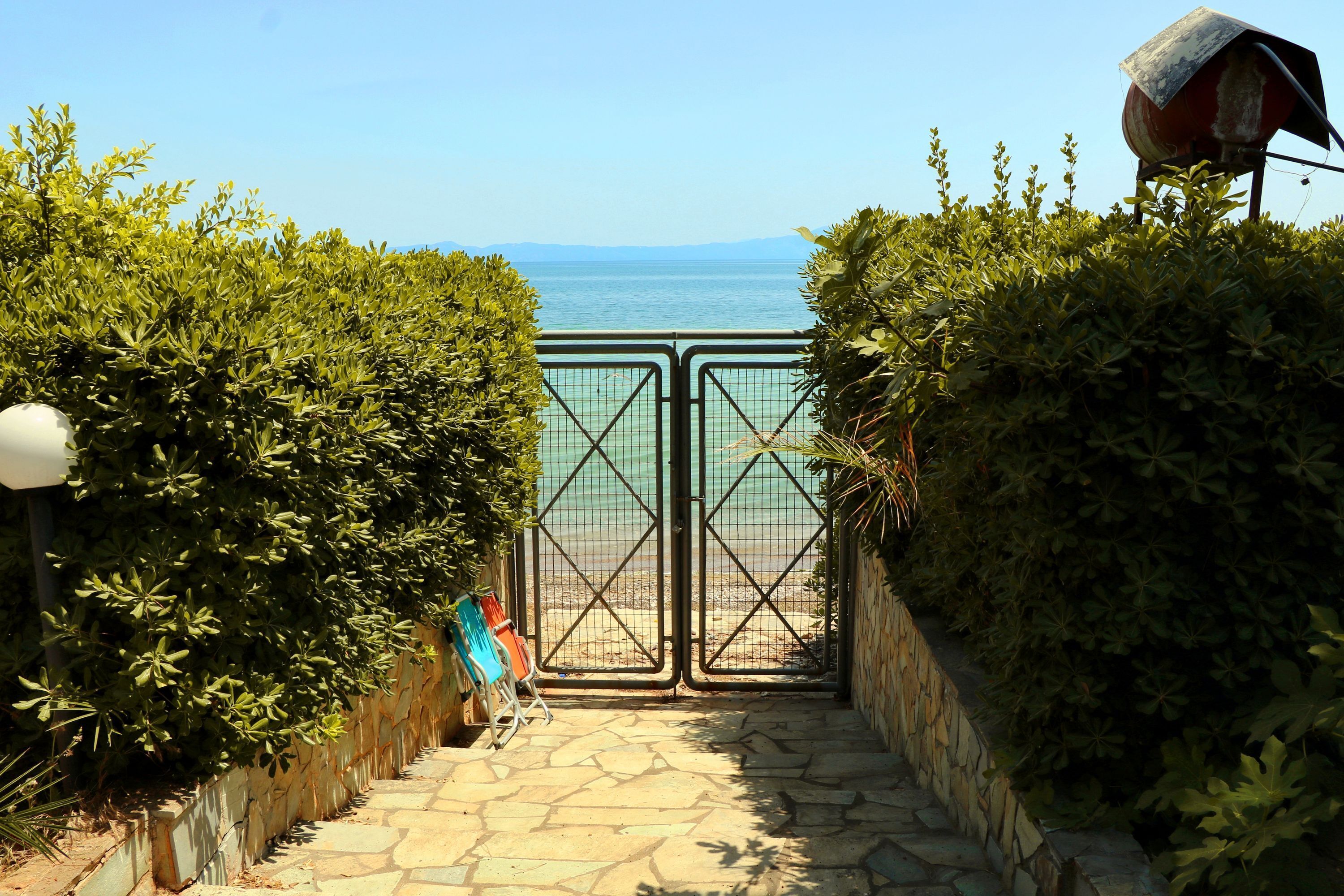 Un chemin de pierre mène à une entrée fermée par un portail, d’où l’on peut admirer la mer.