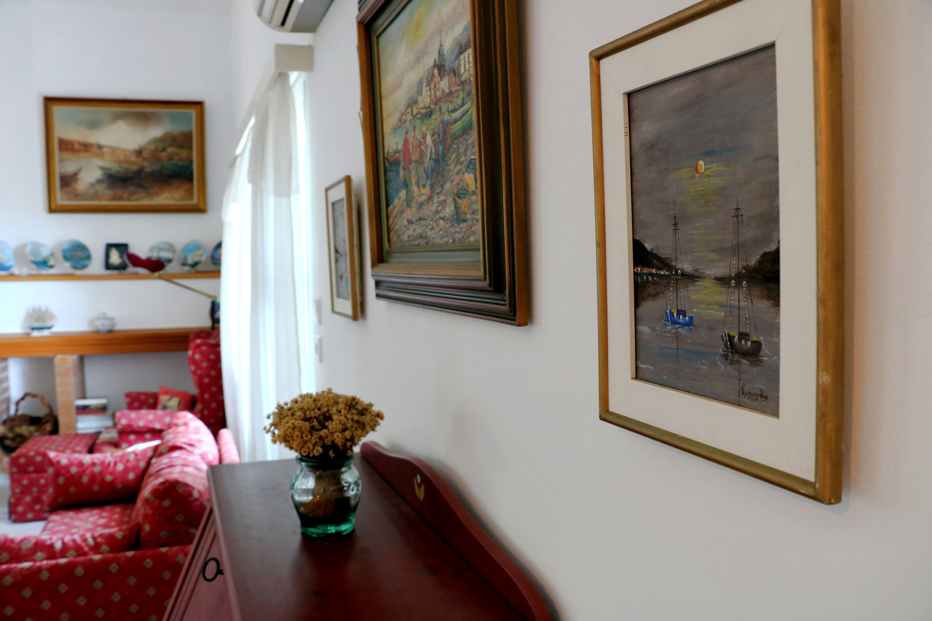 Une pièce avec un canapé rouge, une table d’appoint en bois sur laquelle se trouve un vase, et des œuvres d’art encadrées accrochées au mur.