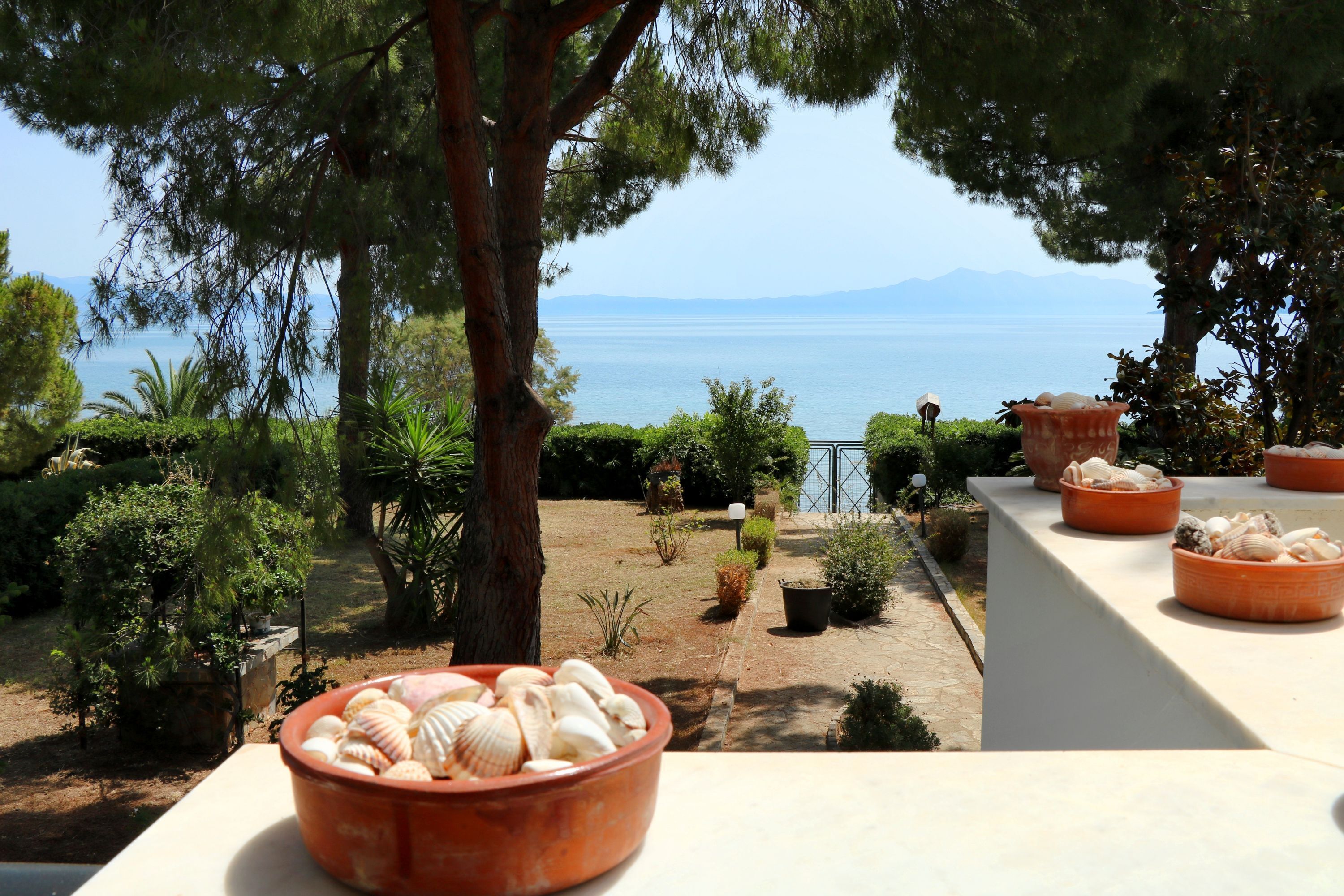 Eine Terrasse mit Terrakotta-Töpfen mit Muscheln, mit Blick auf einen Garten mit verschiedenen Pflanzen und Meerblick.