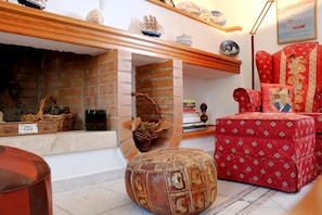 Un salón acogedor con chimenea, un otomano rojo estampado y un sillón tapizado en rojo.