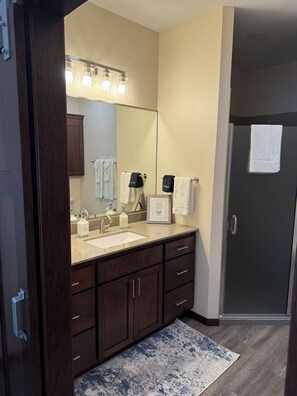 A bathroom with a large mirror, a sink, and a dark wooden vanity. There are towels hanging on the wall and a framed thank you card on the counter.