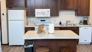 A kitchen with wooden cabinets, a white refrigerator, a microwave, a toaster, a sink, and two stools.