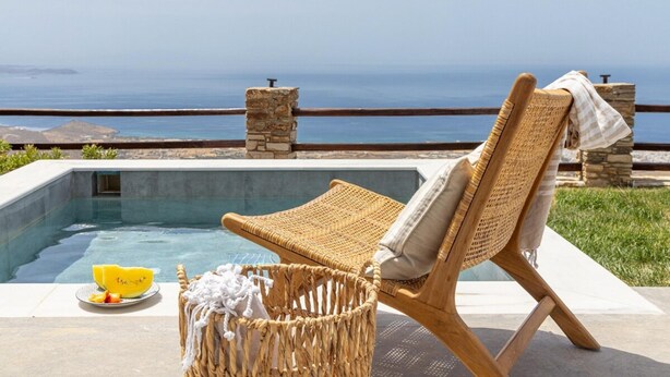A wicker lounge chair by a pool with a stone pillar and a view of the sea. - Del Sol View, Arnados Tinos (Arnados)