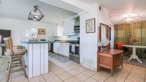 Cocina moderna con armarios blancos, una isla central y electrodomésticos de acero inoxidable. Hay una zona de comedor con una mesa y sillas, y una pequeña planta decorativa sobre la mesa.