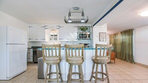 Una cocina con armarios blancos, una isla central con taburetes de bar, un refrigerador y un microondas.
