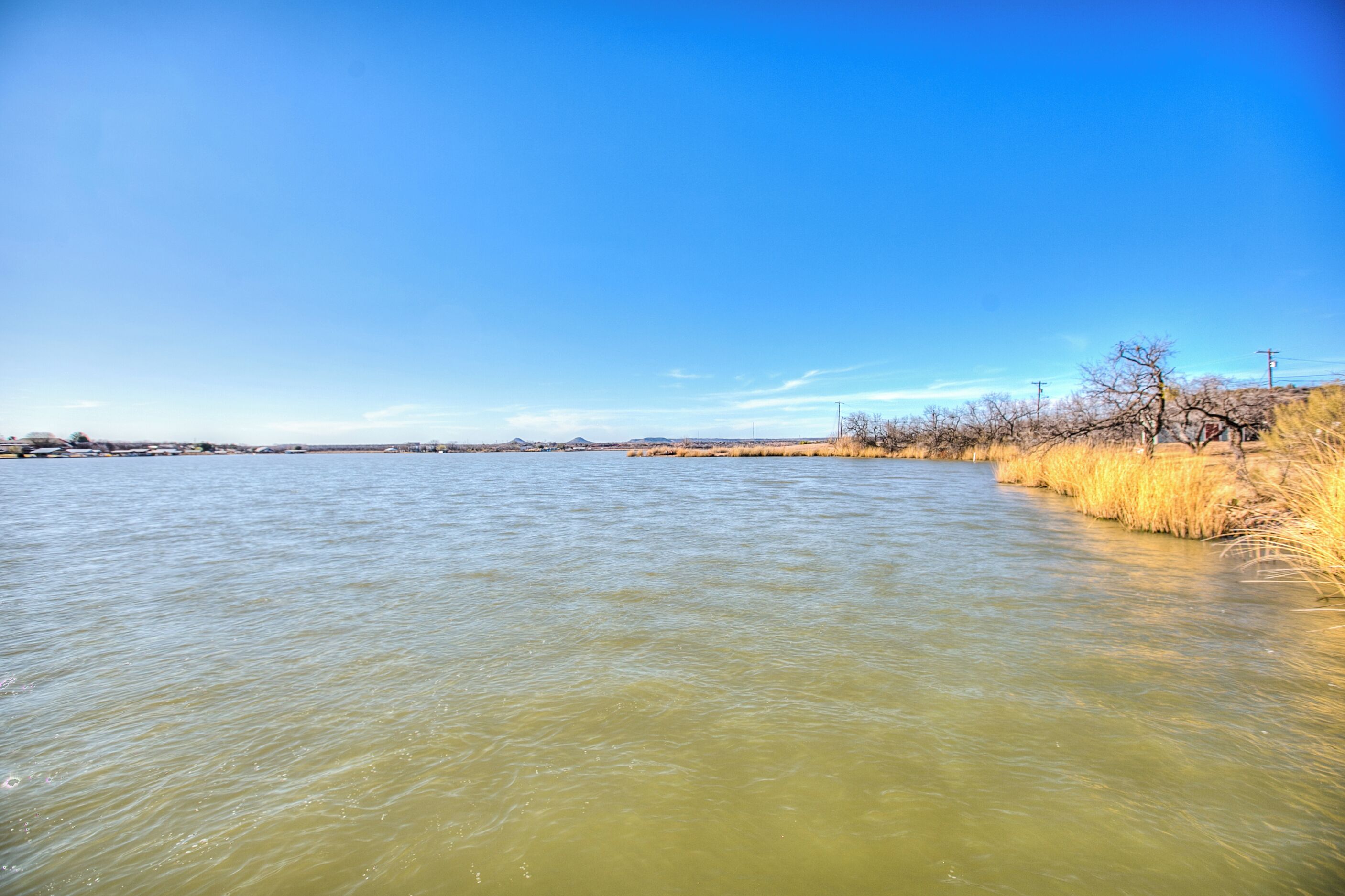 A river with a clear sky and dry grass along the bank.