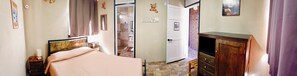 A bedroom with a bed, a wooden dresser, a bathroom visible through an open door, and a wall-mounted light fixture. - Cuanax Hotel (Pozos)