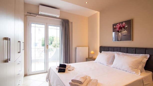 A hotel room with a bed, a nightstand with a lamp, a painting on the wall, and a view of the outdoors through the door.