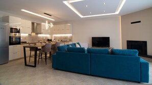A modern kitchen with a dining area, a blue sofa, and a TV in a living room.
