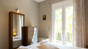 Un dormitorio con un espejo grande, un armario de madera, una mesita de noche con una lámpara y vistas a un jardín a través de una puerta de vidrio corredera.