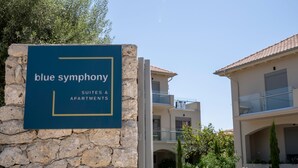 Une enseigne indiquant « Blue Symphony Suites & Apartments », avec un mur en pierre et une vue sur la façade de l’immeuble.