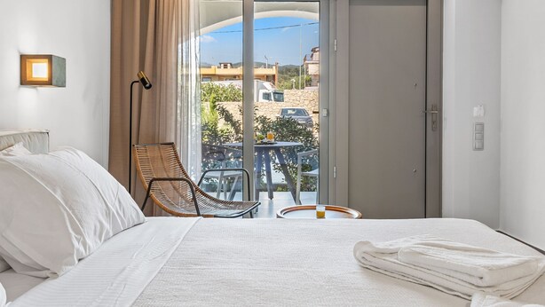 Une chambre d’hôtel avec un lit, une chaise, une table avec un verre et une vue sur l’extérieur.
