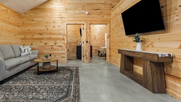 A log cabin interior with a sofa, coffee table, rug, fireplace, and a mounted TV. - Acadia Timber Cottages #55 - Minutes to Acadia National Park! (Trenton)