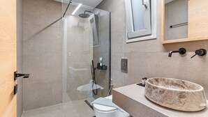 A modern bathroom with a glass-enclosed shower, a white toilet, and a beige stone sink. - garden & pool view Ground floor (Nikiana)