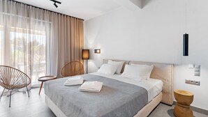 A modern bedroom with a large bed, two chairs, a bedside table, and a wall-mounted light fixture. - garden & pool view Ground floor (Nikiana)