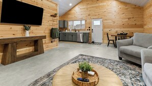 A cozy cabin interior with a living room, kitchen, and dining area, featuring wooden walls and a sloped ceiling. - Acadia Timber Cottages #51 - Minutes to Acadia National Park! (Trenton)