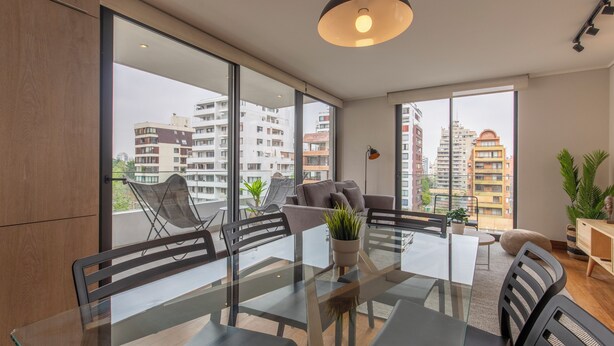 Un salon moderne avec une table à manger en verre, des sièges confortables, de grandes fenêtres et une vue sur le paysage urbain.