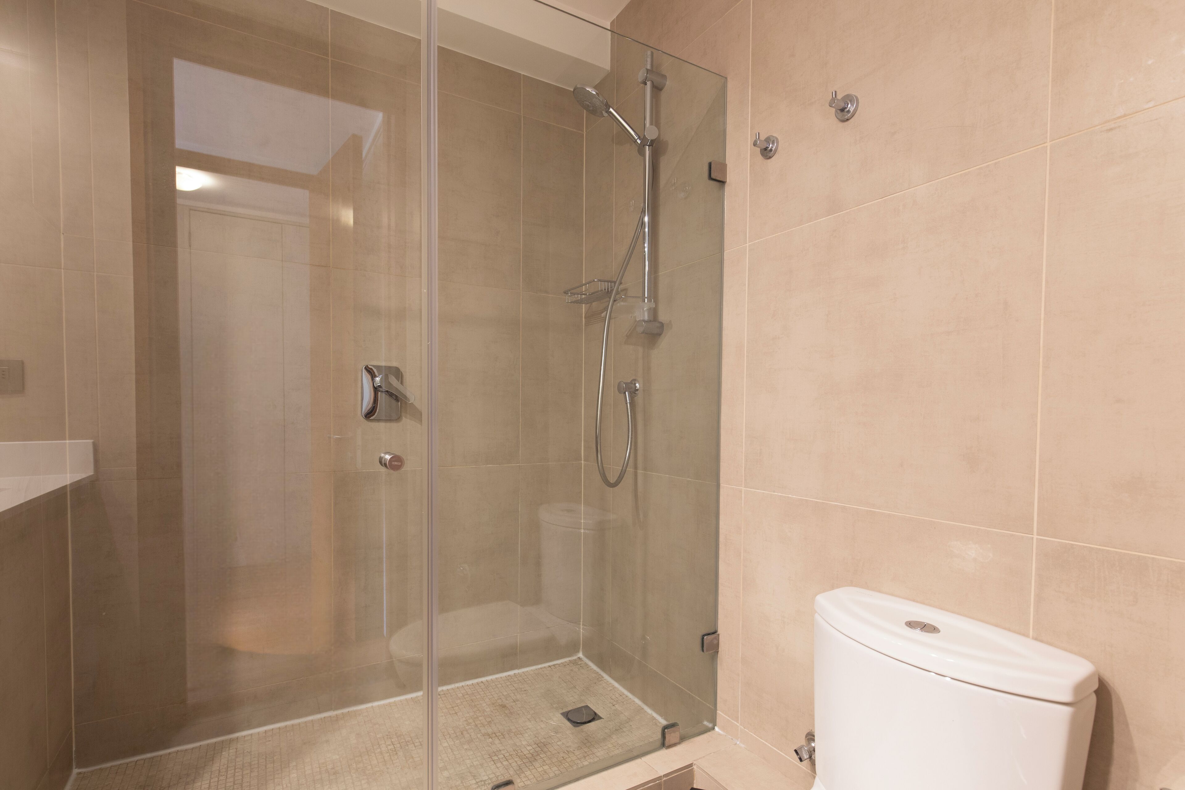 Une salle de bain moderne avec une douche à parois de verre, des toilettes blanches et des carreaux de couleur beige.