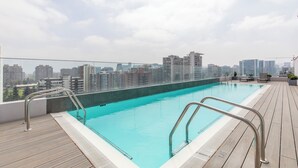 Une piscine sur le toit offrant une vue sur la ville, avec des garde-corps en métal et une terrasse en bois.