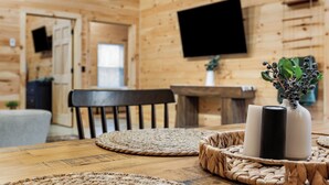 A wooden cabin interior with a dining table, chairs, a TV mounted on the wall, and a small plant on the side. - Acadia Timber Cottages #58 - Minutes to Acadia National Park! (Trenton)
