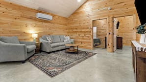 A cozy room with wooden walls, a grey sofa, a patterned rug, and a small table. - Acadia Timber Cottages #58 - Minutes to Acadia National Park! (Trenton)