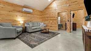 Een knus vertrek met houten wanden, een grijze bank, een kamerbreed tapijt en een kleine tafel.