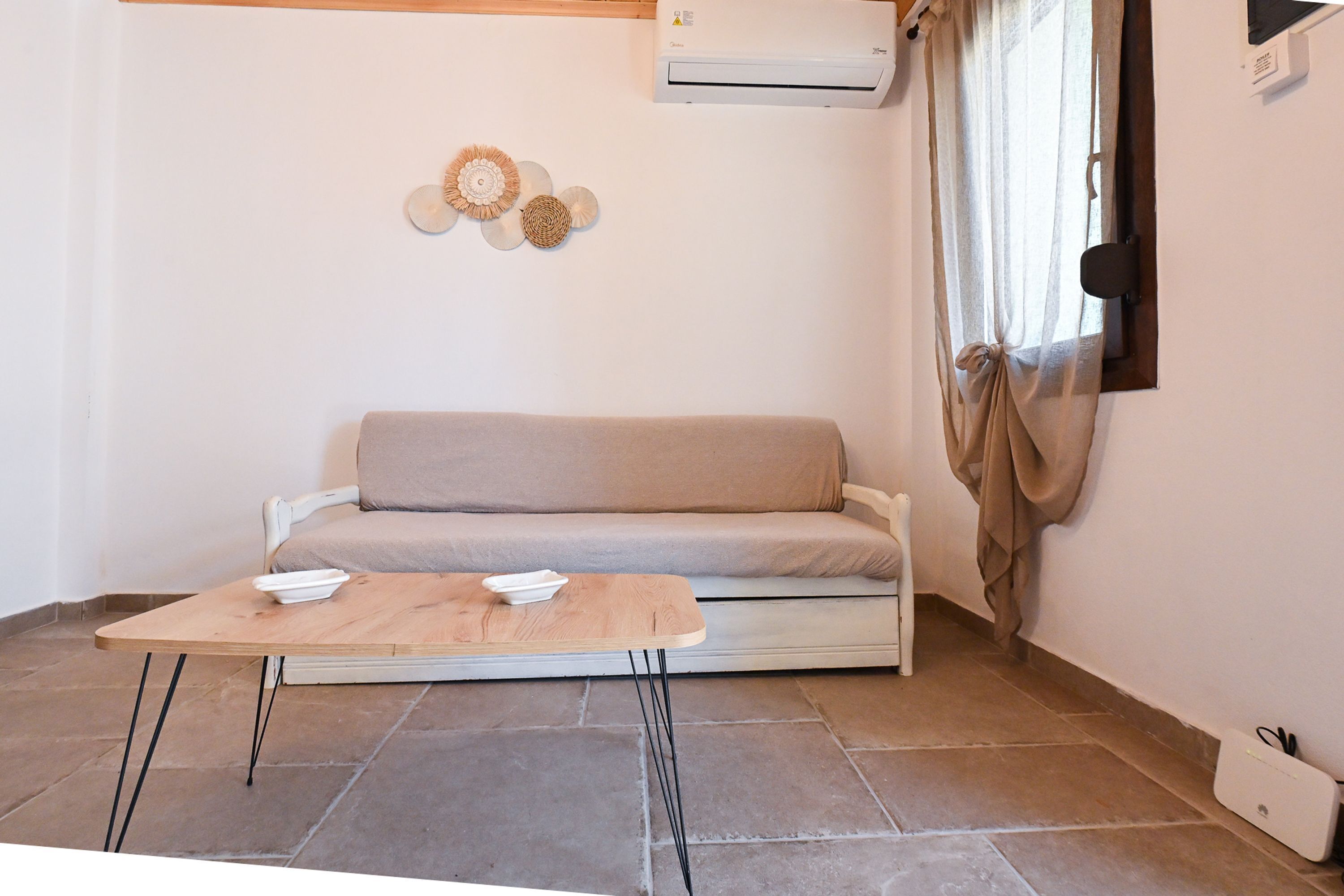 A room with a sofa, a small wooden table, an air conditioner, and a wall-mounted speaker.