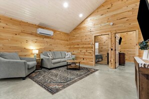 Ein gemütliches Zimmer mit Holzwänden, einem grauen Sofa, einem gemusterten Teppich und einem kleinen Tisch.