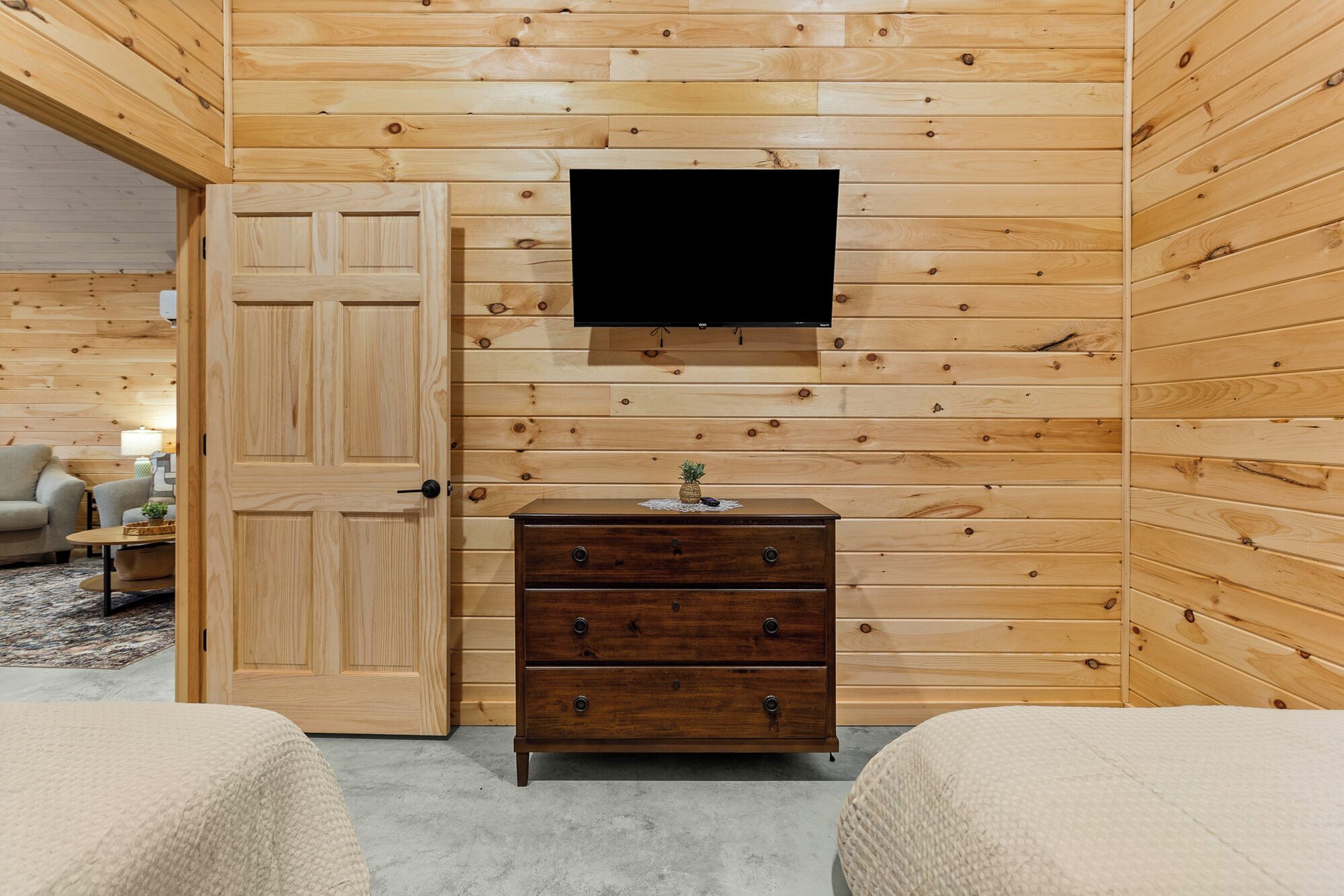 A wooden-paneled room with a TV mounted on the wall, a wooden dresser, and two beds.