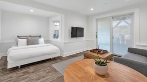 A modern bedroom with a bed, a TV, a window, and a balcony. - The Ocean's Edge Studio (SF)