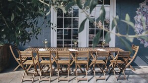 An outdoor wooden table and chairs set against a blue wall with windows. - The Ocean's Edge Studio (SF)