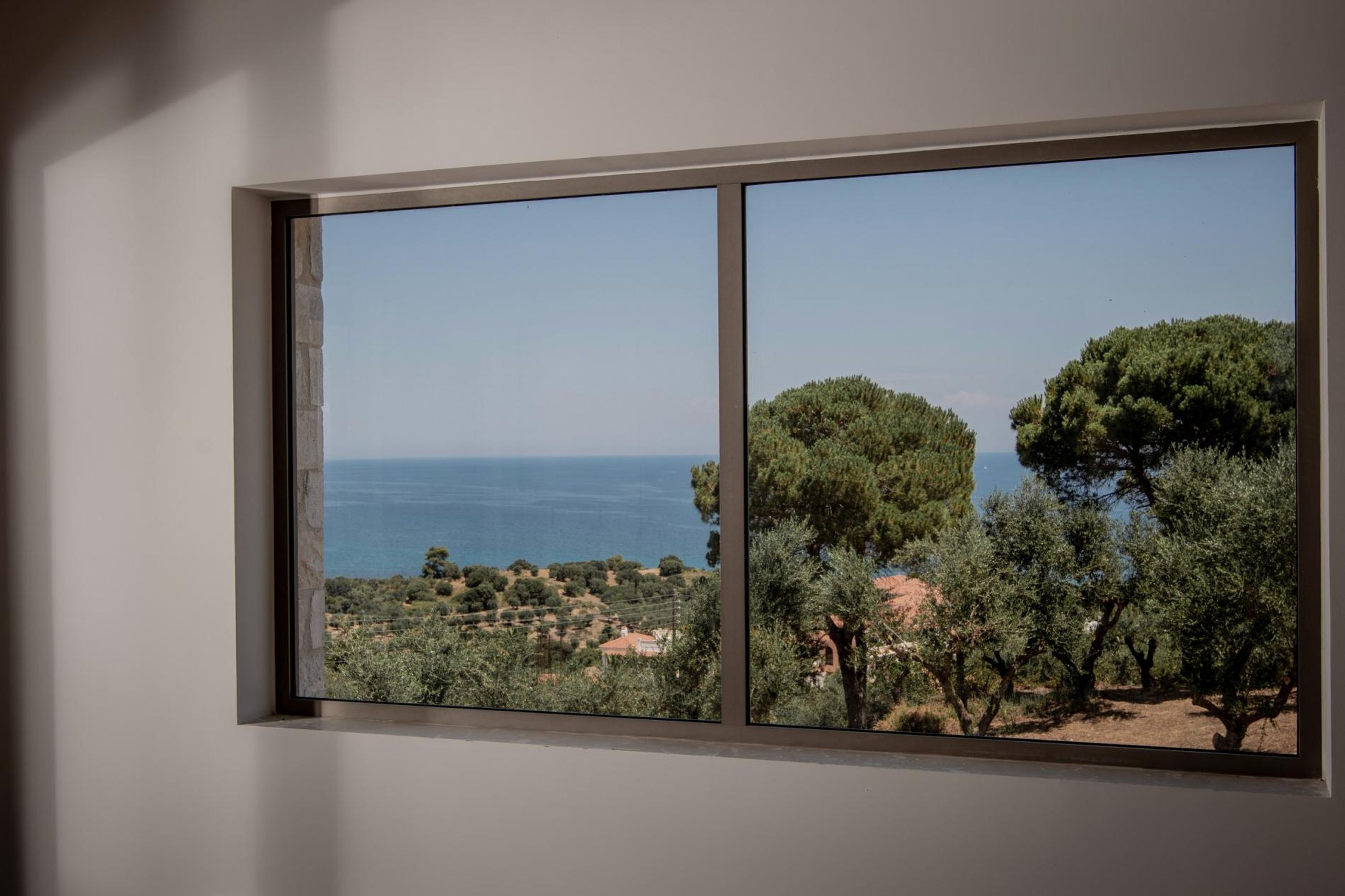 Une fenêtre donnant sur un paysage côtier, avec des arbres et la mer en vue.