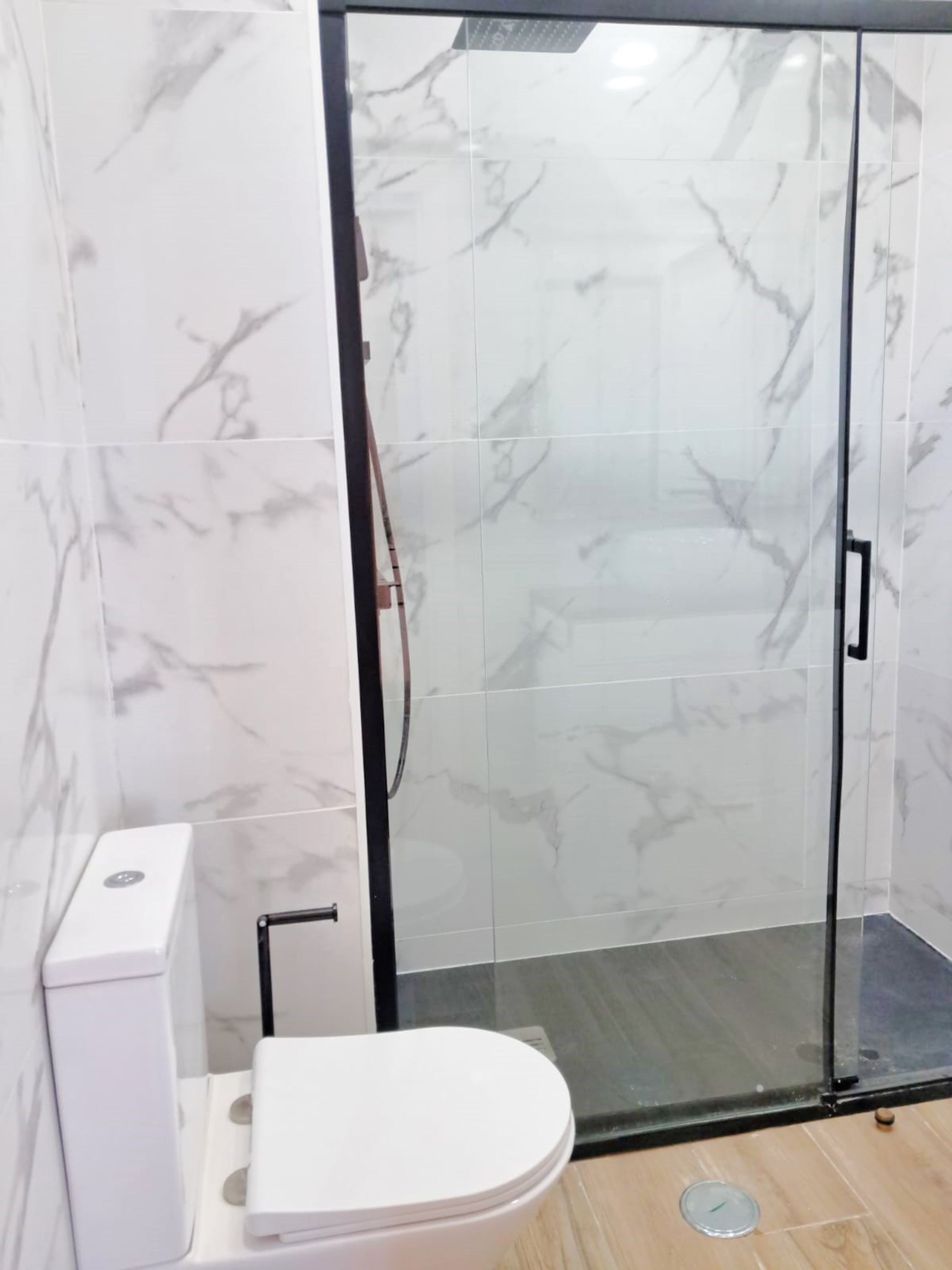 A bathroom with a toilet, a glass shower enclosure, and marble-patterned walls.