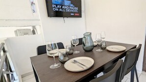 En matplats med ett bord dukat för fyra personer, med glas, tallrikar och bestick. En tv är monterad på väggen och visar en reklamfilm.