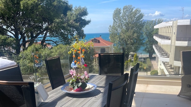 En uteplats med ett bord och stolar, en blomsterarrangemang och utsikt över havet och byggnaderna.