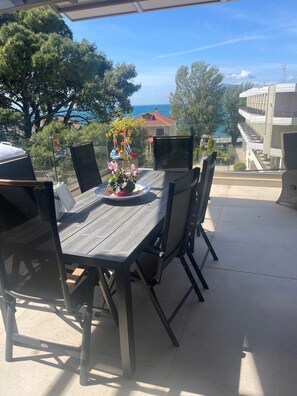 An outdoor patio with a table and chairs, a flower arrangement, and a view of the sea and buildings. - Sea View Apartment Patras (Patra)