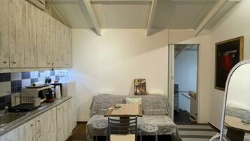A compact living space with a kitchenette, a sofa, a dining table, and a pet bed.