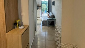A hallway leading to a bedroom with a bed, a small table, and a chair. There is a radiator on the right and a wooden cabinet on the left. - Simple Stay  Vari's House (Vari)