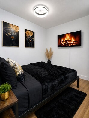 Ein modernes Schlafzimmer mit einem schwarzen Bett, einem Flachbildfernseher und zwei gerahmten Kunstwerken.
