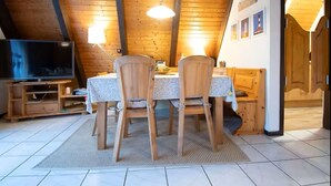 A cozy dining area with a wooden table and chairs, a television on a stand, and a ceiling light. - Family-friendly vacation home in Burhave - 500 m to the beach, WLAN, garden (Burhave)
